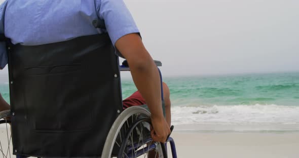 Rear view of African American man sitting on wheelchair at beach 4k