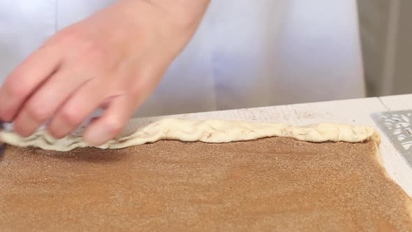 The Woman Rolls The Cinnabon Dough, Sprinkled With Cinnamon. On A White Tabletop. Close Up Shot.
