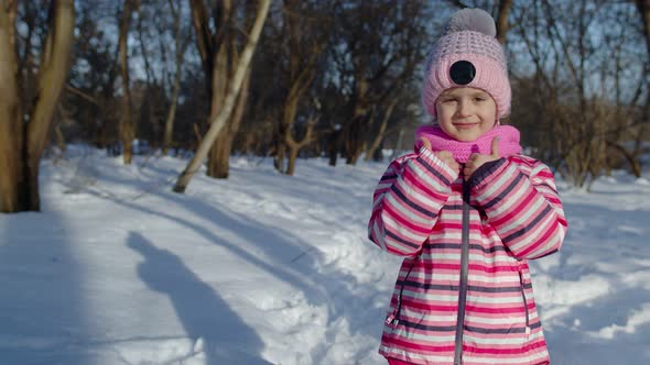 Joyful Little Child Girl Smiling Showing Thumbs Up Gesture on Snowy Road in Winter Park Outdoors