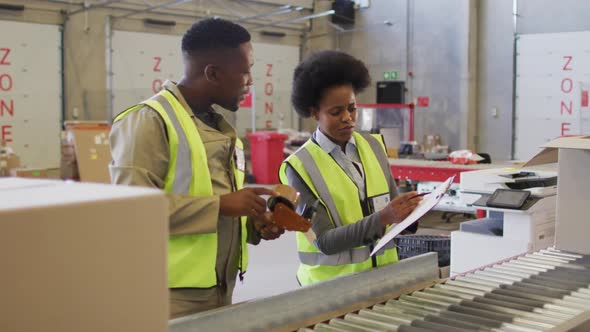 African american male and female workers with clipboard next to conveyor belt in warehouse