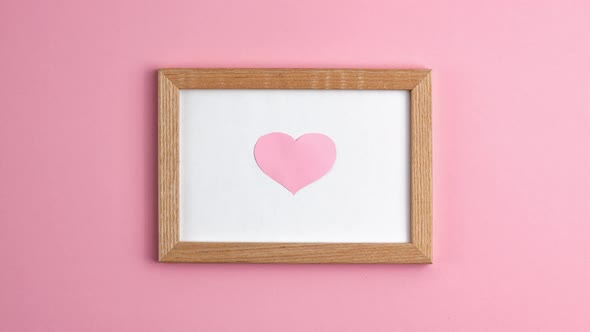 Stop motion animation of pink paper hearts in wooden frame on pink background at the centre side