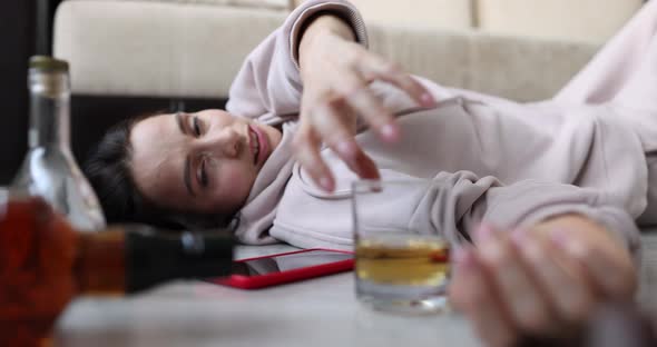 A Woman on the Couch Holds Out Her Hand to a Glass of Alcohol