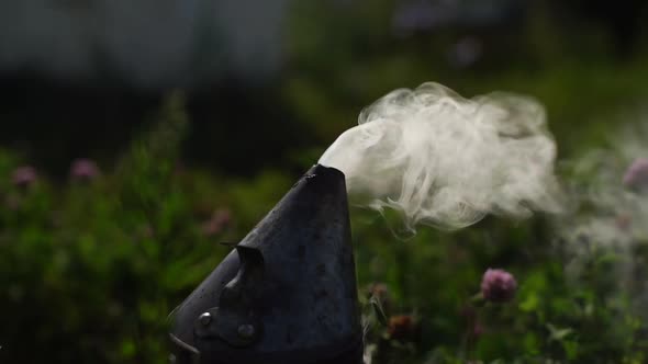 Closeup of Bee Smoker Blowing Smoke in Wind Against Background of Green Grass and Bright Sunlight
