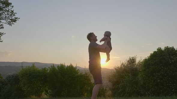 Strong-willed Father Throwing and Catching His Jolly Baby Boy on a Sunset