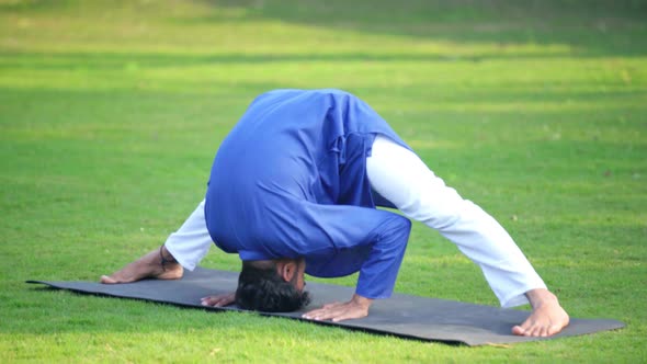 Indian man doing Wide Legged Forward Bend Yoga pose or Prasarita Padottanasana in Kurta Pajama