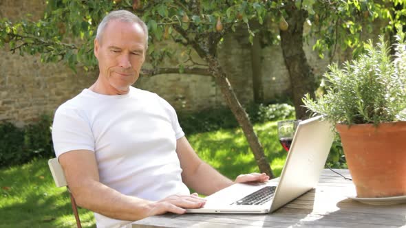 MS, Senior male sitting at table in garden working on laptop