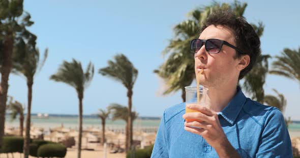 Man on Vacation Backdrop of Palm Trees Sea Drinks Orange Cocktail Enjoying Summer Holiday at