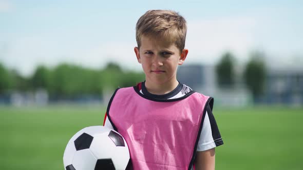 Portrait of a Football Player Boy, a Young Boy Stands Near a Football Field and Looks at the Camera