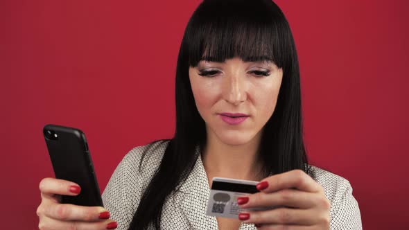 Darkhaired Young Woman 30 Years Old Makes a Purchase Via the Internet While Holding a Smartphone