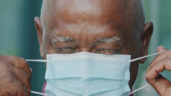 Crop Closeup of Mature Man Putting on Protective Surgical Facial Mask African American Elderly