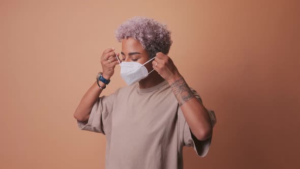 Smiling Young African American Woman with Blonde Hair Puts on Face Medical Mask