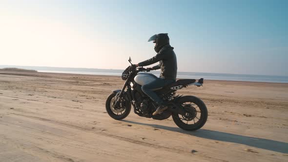 Motorcyclist Driving His Customized Fast Motorbike on the Dirt Road in Desert Around Sea or Lake
