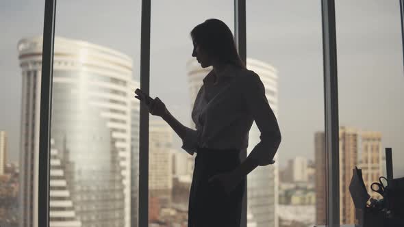 Silhouette of a Young Woman Against the Background of a Large Window and Skyscraper