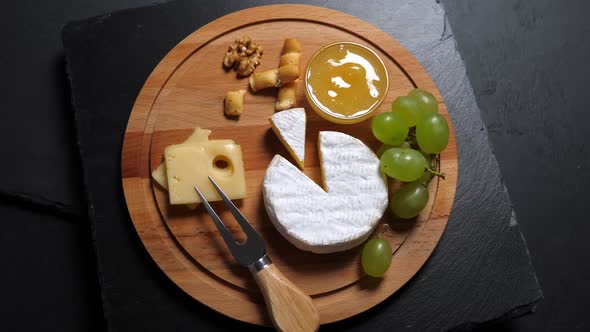 Sliced Cheese,nuts, Grape, Honey and Knife on Wooden Platter. Rotating