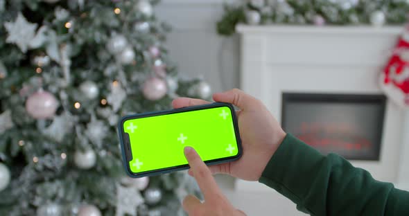 Closeup of Male Hands Holding Black Modern Smartphone in Hands at Glowing Christmas Home Interior