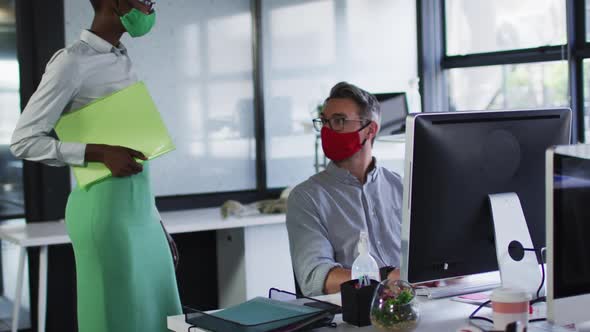 Diverse male and female office colleagues wearing face masks greeting each other by touching elbows