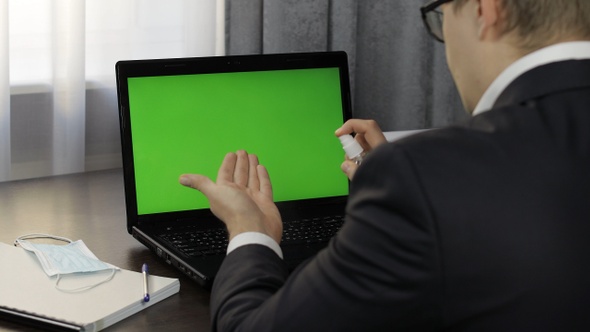 Man Takes Sanitizer Bottle and Use Near Laptop with Green Screen. Distance Work