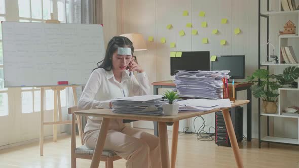 Sick Asian Woman Talking On Phone And Taking Note While Working Hard With Documents At Office