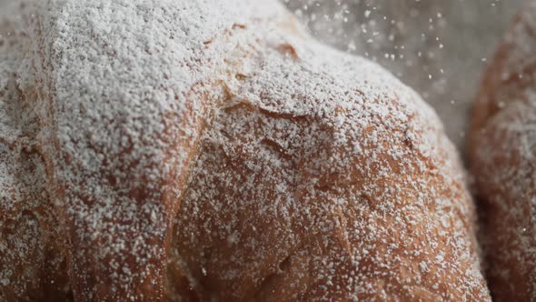 Camera follows sprinkling powered sugar over croissant. Slow Motion.