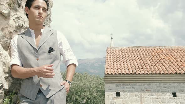 Attractive young fashion man in a suit walks around the old town along the plants. Slow motion