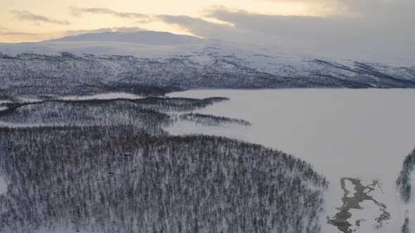 Aerial view flying across beautiful snowy freezing evergreen woodland across Scandinavian mountain l