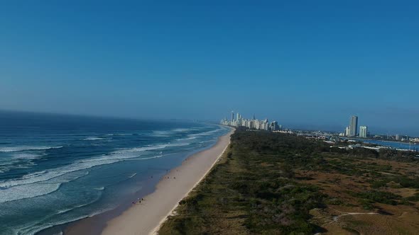 Aerial view of a popular beach near a large area of green space with a sprawling city skyline in the