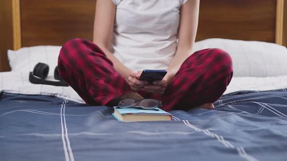  woman in glasses typing sms on phone and gathering to read book in contemporary bedroom