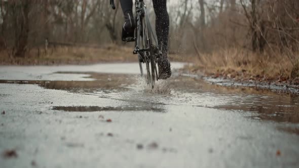 Water Spray From Bicycle Wheel. Cyclist Riding On Road Bike. Bike Wheels Rides Through Puddle.