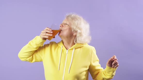 Cheerful Old Lady in a Yellow Sports Sweater Enjoys Fresh Carrot Juice