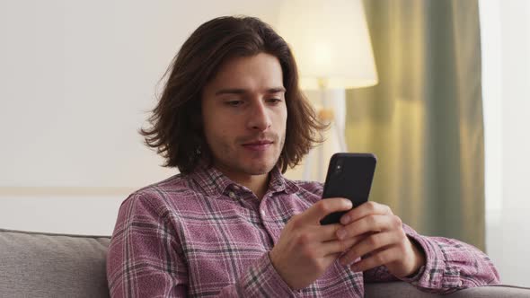 Close Up of Young Man Sitting on Couch at Home Web Surfing in Social Media on Smartphone