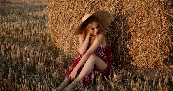 Pretty Girl Sitting In A Field Near A Haystack