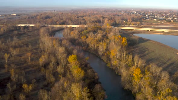 Drone shot of a river flowing under a highway overpass during a warm sunrise.