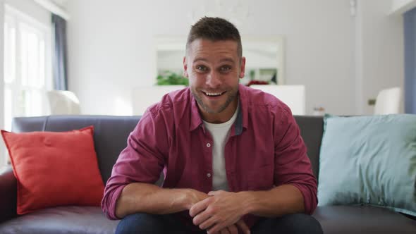 Happy caucasian man at home, sitting on couch making video call, talking and smiling