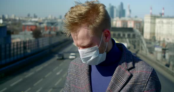 Portrait of a Man on a City Street, He Puts a Disposable Mask on His Face, Holds a Smartphone