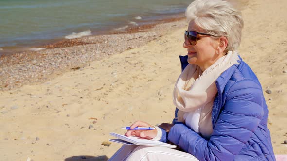 Senior Woman Writing To Notebook on Summer Beach