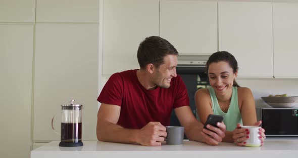 Happy caucasian couple drinking coffee and using smartphone