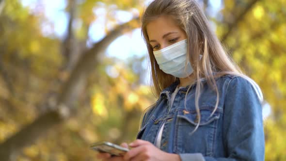 Portrait Woman in Protective Medical Mask Walks Down To the Street Uses Phone Texts Scrolls Surfs