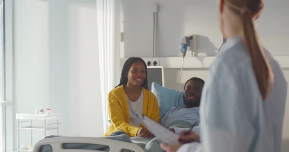 Female Doctor Talking To Africanamerican Couple in Hospital Room