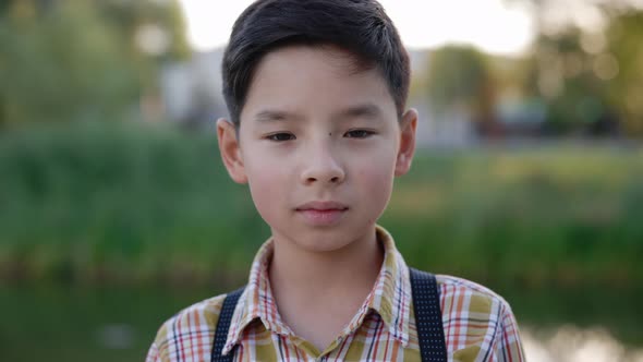 Close Up of the Asian Boy Standing Near Beautiful Lake Looking at the Camera Wearing Special Fishing