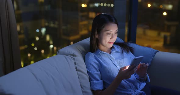 Woman watch at cellphone and sit on sofa in the evening