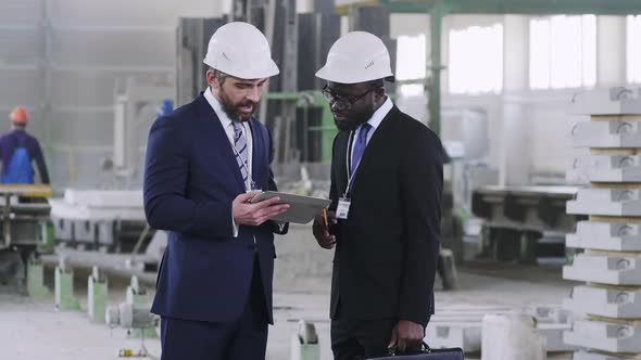 Diverse managerial personnel staying at factory with tablet computer