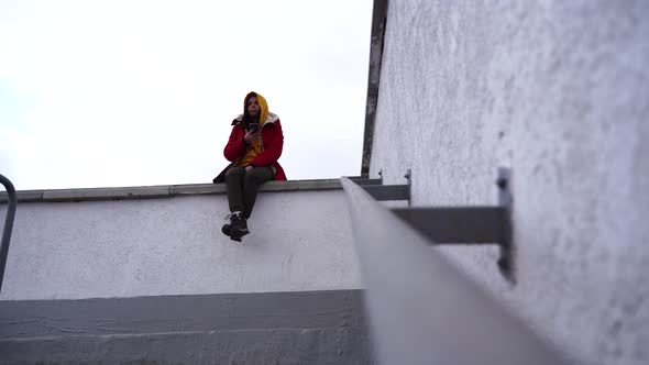 Young Woman with Mobile Phone Sitting on Concrete Parapet