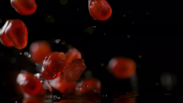 Pomegranate seeds falling on water surface. Slow Motion.