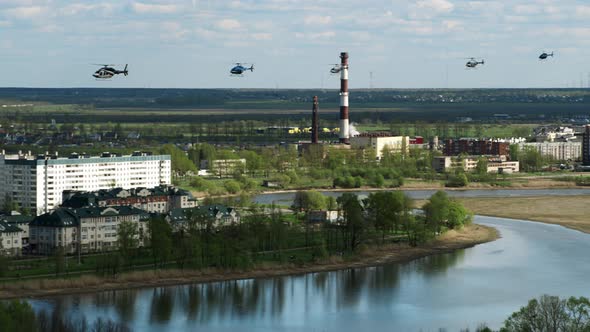 Six Helicopters Fly One After Other Over Houses and Next to River on a Sunny Summer Day