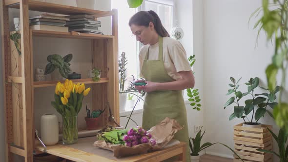 A Woman Florist in Glasses and an Apron Works Behind the Counter in a Flower Shop