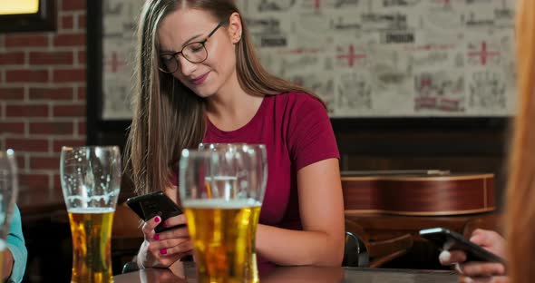 Woman is Typing a Message on a Smartphone in a Bar While a Glass of