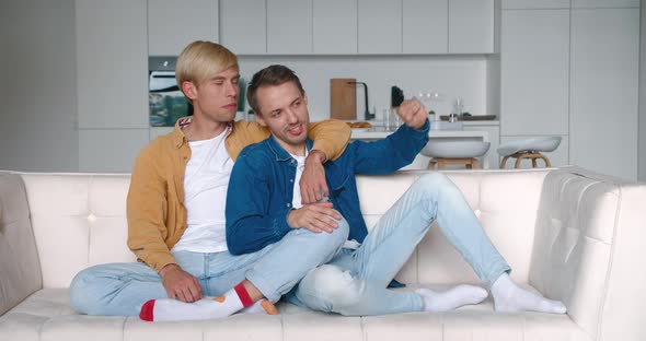 Happy Men Homosexual Couple Sit at Home Together on Their Sofa in an Embrace