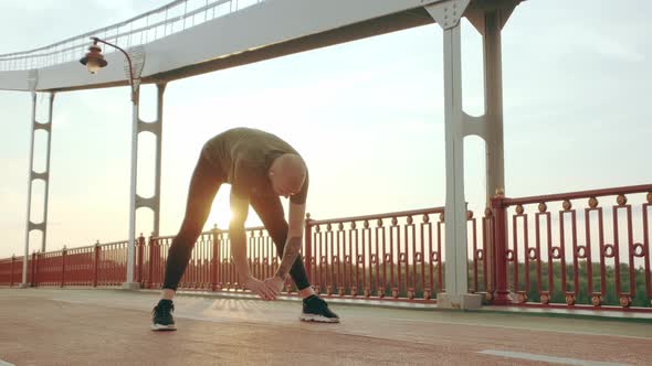 Young White Man in Black Sport Uniform Doing Warmup Before Run Pedestrian Bridge at Dawn