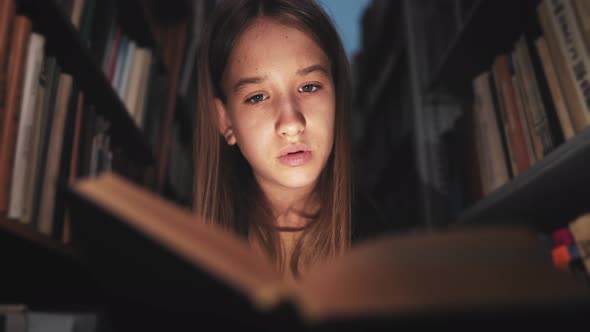 Girl in Library Between the Bookshelves and Reading Book Aloud for Finding Information