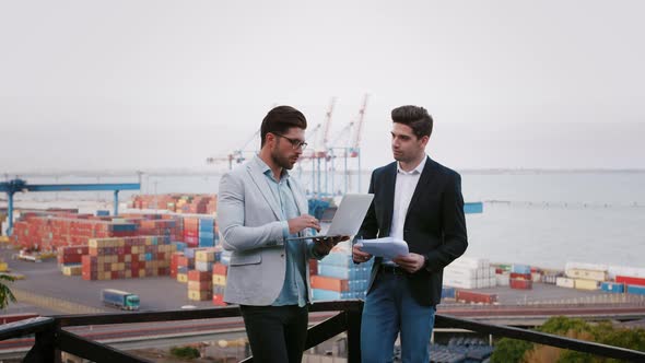 Two Business Partners Discussing the Meeting with Laptop and Contract Outdoors on Background of the